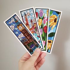 a hand holding four stained glass stickers in front of a white wall with flowers on it