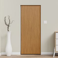 a white vase sitting next to a wooden door in a room with gray walls and wood flooring