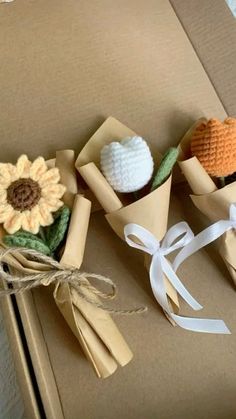 three small crocheted flowers are sitting in a box with twine ribbons on it