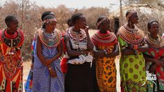 four african women dressed in colorful clothing and headdress, with sticks on their heads