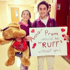 a man and woman holding up a sign with a teddy bear in front of them