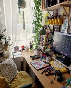 a desk with a computer monitor, keyboard and various office supplies on it in front of a window