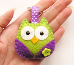 a small green and purple owl keychain on someone's hand with it's eyes wide open