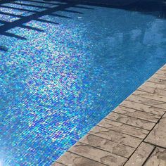 an empty swimming pool next to a stone walkway and water feature with sun shining through the window