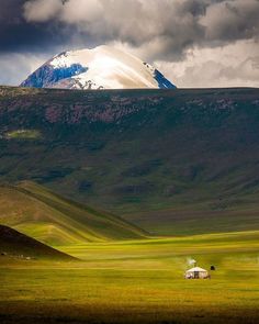 a small house in the middle of a field with mountains in the backgroud