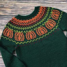 a green sweater with an orange and red design on the front, sitting on a wooden surface