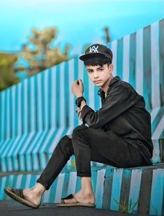 a young man sitting on top of a wooden bench next to a blue and white fence