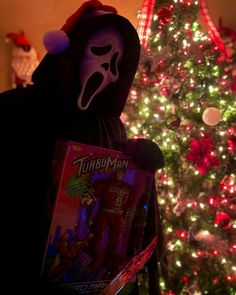 a person wearing a mask holding a box in front of a christmas tree