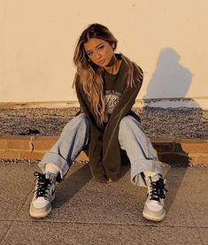 a young woman sitting on the ground with her legs crossed and wearing sneakers, looking at the camera