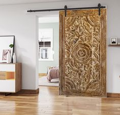 an ornate wooden door is opened to reveal a bedroom with white walls and wood floors