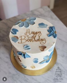 a white and blue birthday cake with flowers on the top is sitting on a marble table