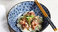 a blue and white bowl filled with rice, meat and veggies next to chopsticks