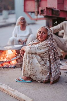 an old woman sitting on the ground next to a fire