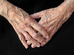 an old woman's hands are folded in the shape of a heart on a black background