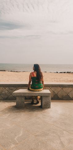 a woman sitting on top of a cement bench next to the ocean in front of a sandy beach