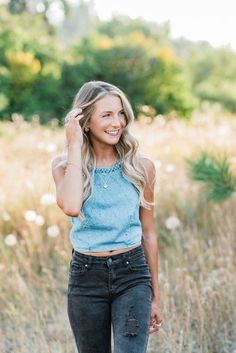 a woman standing in the middle of a field wearing black jeans and a blue tank top