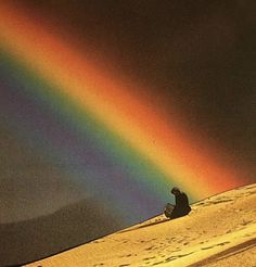 a person sitting in the snow under a rainbow