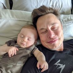 a man laying on top of a bed holding a sleeping baby in his arms and smiling at the camera