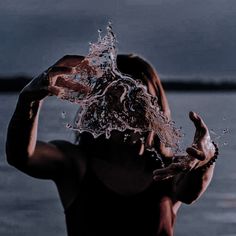 a woman is holding her head in the air with water splashing on her face