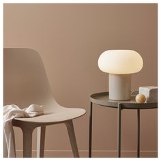 a white table lamp sitting on top of a wooden table next to a gray chair