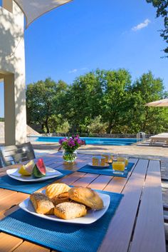 a plate of bread and watermelon sit on a table near an outdoor swimming pool