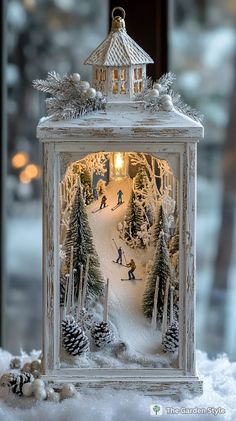 a small white lantern with snow on the ground and trees around it, in front of a window