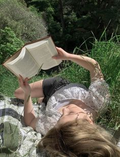 a woman laying on the ground reading a book in her hands while holding an open book