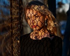 a woman standing behind a fence with her hair blowing in the wind