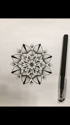 a black and white drawing of a flower on paper next to a marker with the ink pen in it