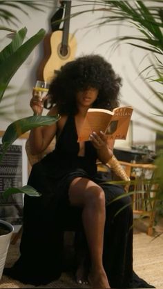 a woman sitting on a chair reading a book and holding a cup in her hand