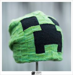 a green and black knitted hat sitting on top of a wooden stand