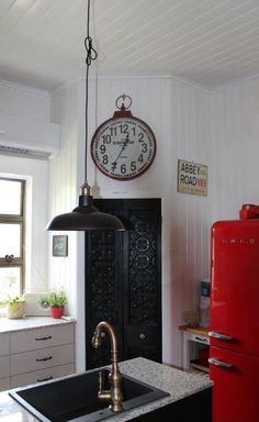 a kitchen with a red refrigerator and clock on the wall above it's sink