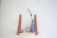 two vases and one flower are on a shelf with other items in front of the wall