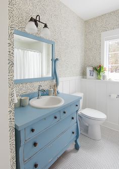 a blue dresser in a bathroom with a white toilet and sink next to a window