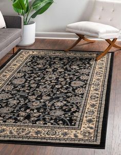 a black and beige area rug with an ornate design on the center, in front of a white chair