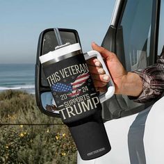 a person holding a coffee mug in front of a truck with the ocean in the background