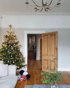 a living room filled with furniture and a christmas tree in front of a doorway that leads to a hallway