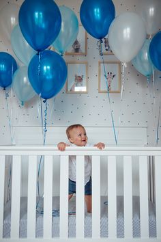 a baby in a crib with blue and white balloons on the wall behind him