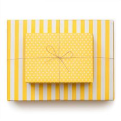 a yellow and white striped gift box with a bow on the top, wrapped in paper