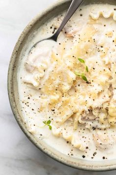 a bowl filled with pasta and sauce on top of a white marble countertop next to a silver spoon