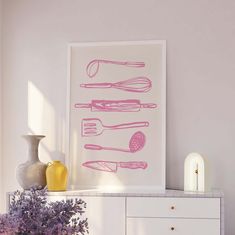 a pink kitchen art print on a white cabinet next to purple flowers and vases