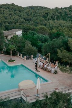 an aerial view of a pool with people sitting at the end and tables set up around it