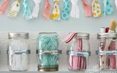 mason jars filled with yarn and toothbrushes are hanging on a wall above a shelf