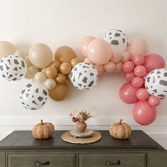 a table topped with balloons and pumpkins next to a wall covered in cow print