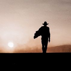 the silhouette of a man in a cowboy hat walking across a field