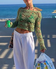 a woman is standing on the beach with her hand in her pocket and holding shopping bags