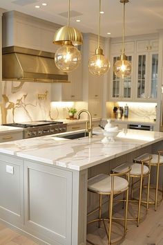 a large kitchen with marble counter tops and gold pendant lights hanging from the ceiling over the island