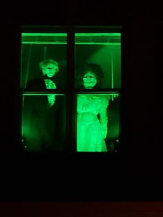 two people dressed as zombies are seen through a window in a dark room with green light