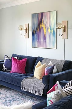 a living room with blue couches and colorful pillows on the sofa, along with two sconces