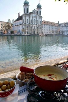 a table topped with bowls filled with food next to a body of water and buildings in the background